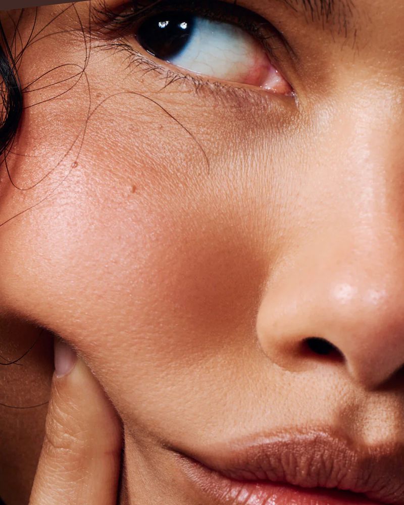 Close-up studio shot featuring an adult female with brown hair, showcasing flawless skin, neutral makeup, and soft, natural lighting.