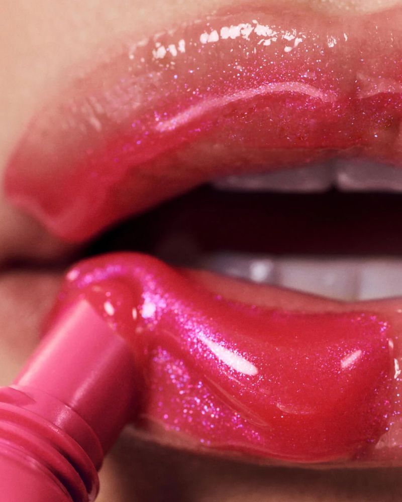 Close-up of a woman's lips being glossed with bright pink, shiny lip gloss, highlighting beauty and makeup application.