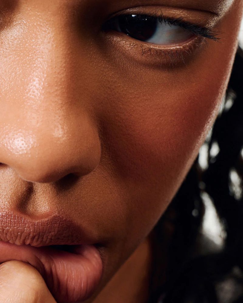 Close-up beauty portrait of a model with warm skin, glowing complexion, and lips touched by fingers for rhode Skin