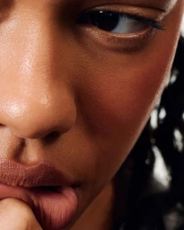 Close-up beauty portrait of a model with warm skin, glowing complexion, and lips touched by fingers for rhode Skin
