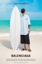 Model wearing dark sunglasses and light blue shirt holding a white surfboard on a sandy beach