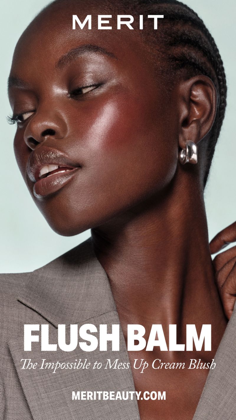 Close-up of an African American woman with braided hair, wearing a gray blazer and silver hoop earrings, showcasing blush makeup.