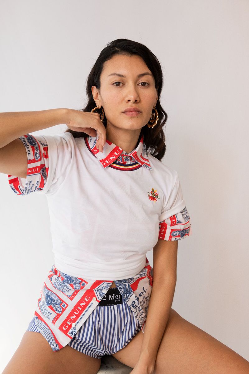 Woman in white polo shirt and striped shorts poses against a white backdrop, showcasing casual and unique fashion style with earrings.