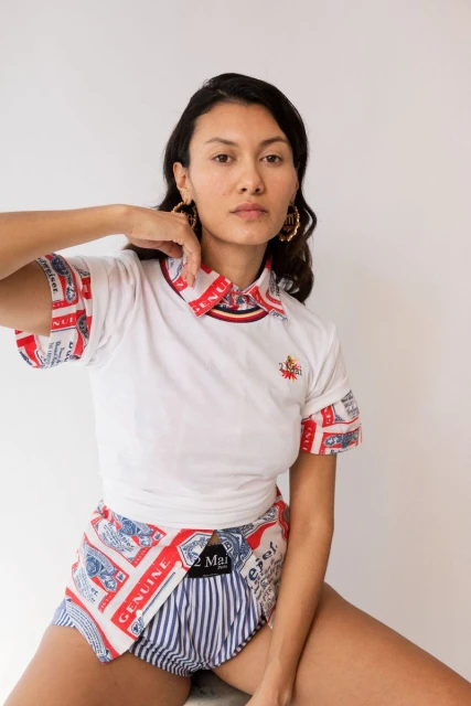 Woman in white polo shirt and striped shorts poses against a white backdrop, showcasing casual and unique fashion style with earrings.