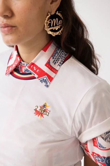 Adult woman wearing gold hoop earrings and white polo shirt with red, white, and blue print collar detail against a white backdrop.