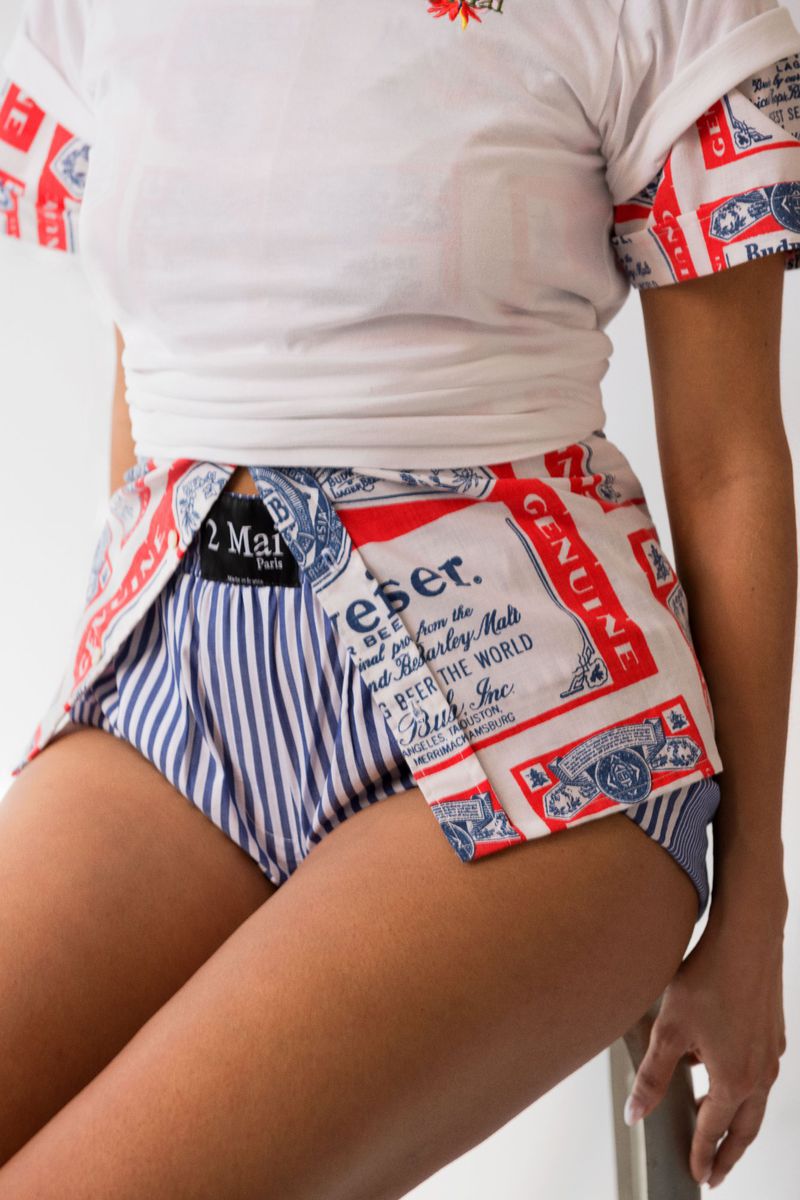 Person wearing a white t-shirt and repurposed beer-branded clothing, including blue and white striped shorts in an indoor setting.