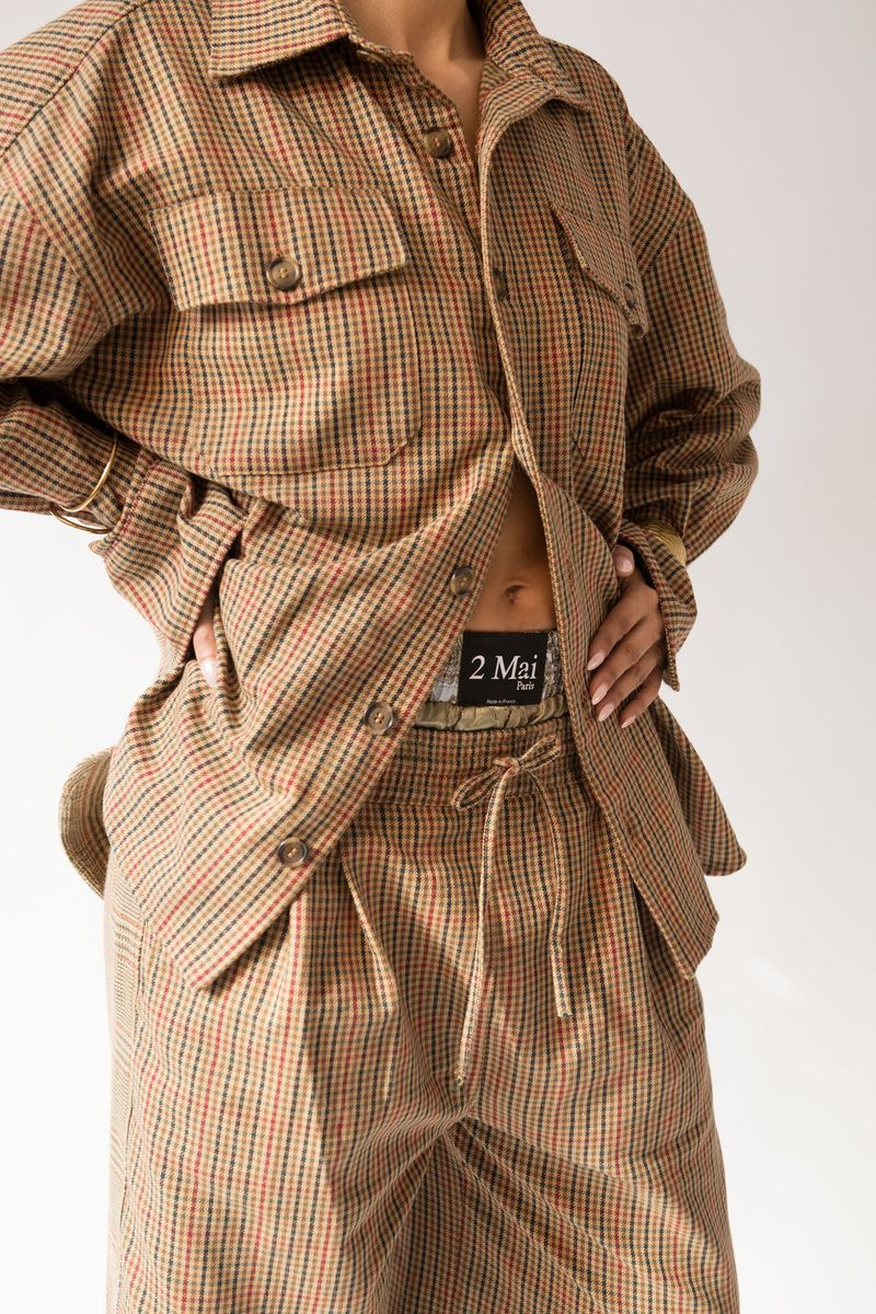A woman poses in a brown plaid two-piece set with a button-down shirt and high-waisted pants against a neutral background.