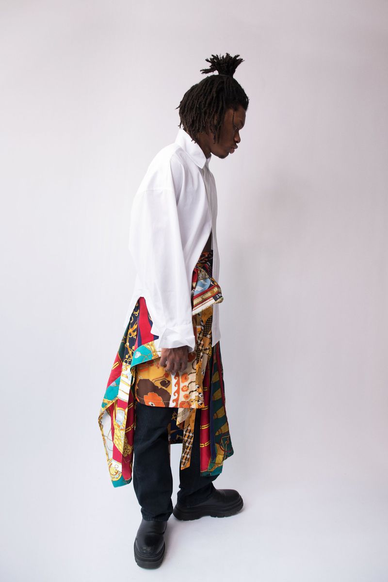 Man wearing a white shirt and patterned scarf tied at the waist against a plain white background