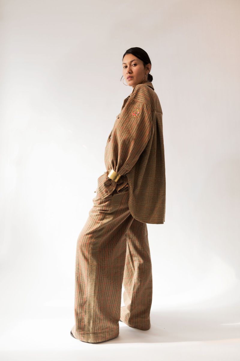 Adult woman in plaid, oversize shirt and pants with gold bracelet in a white studio. Fashion editorial. Wide leg pants, hoop earrings.