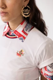 Close up of a woman wearing large gold hoop earrings and a white t-shirt with patterned red and blue collar against a white background