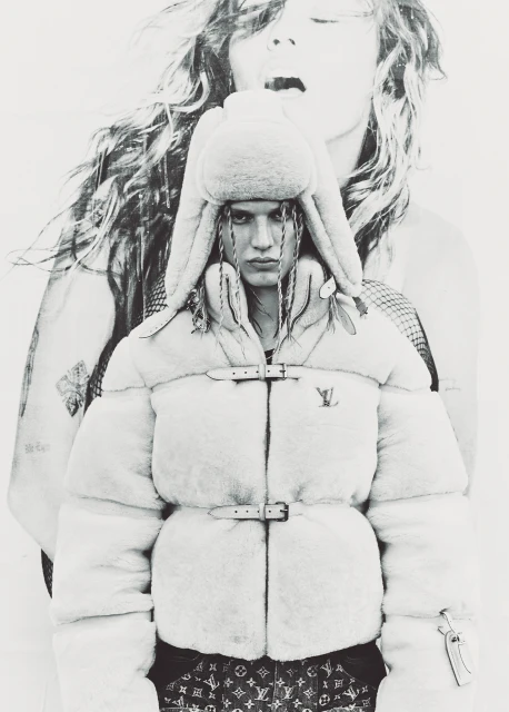 Monochrome fashion shot of a woman in a faux fur jacket and hat, set against a large portrait of a woman with flowing hair.