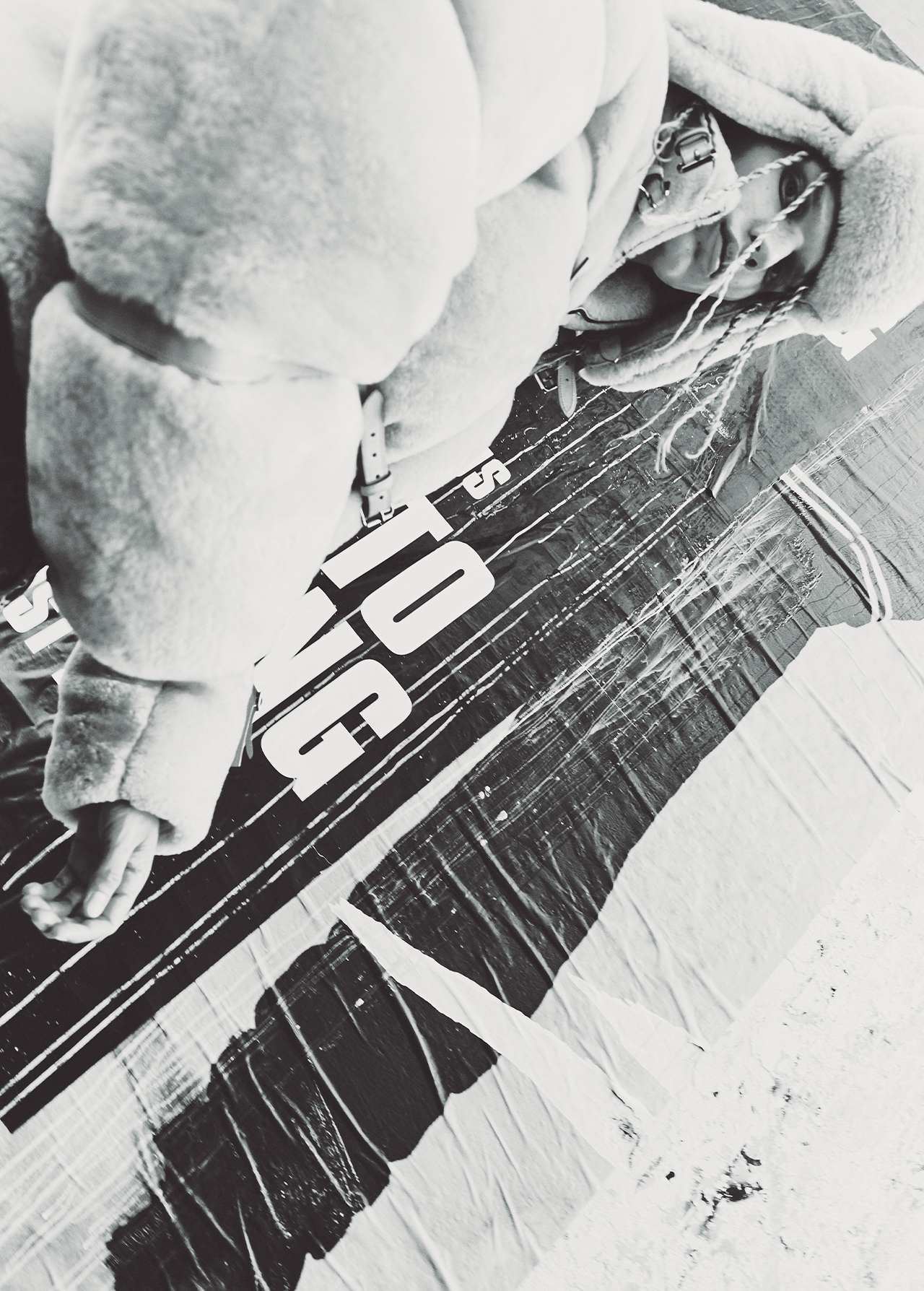 Monochrome portrait of a person in a hooded puffer jacket lying over a textured banner on the ground