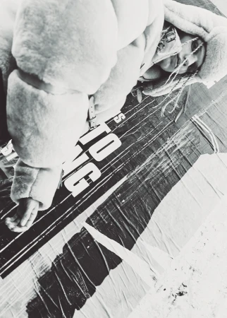 Monochrome portrait of a person in a hooded puffer jacket lying over a textured banner on the ground