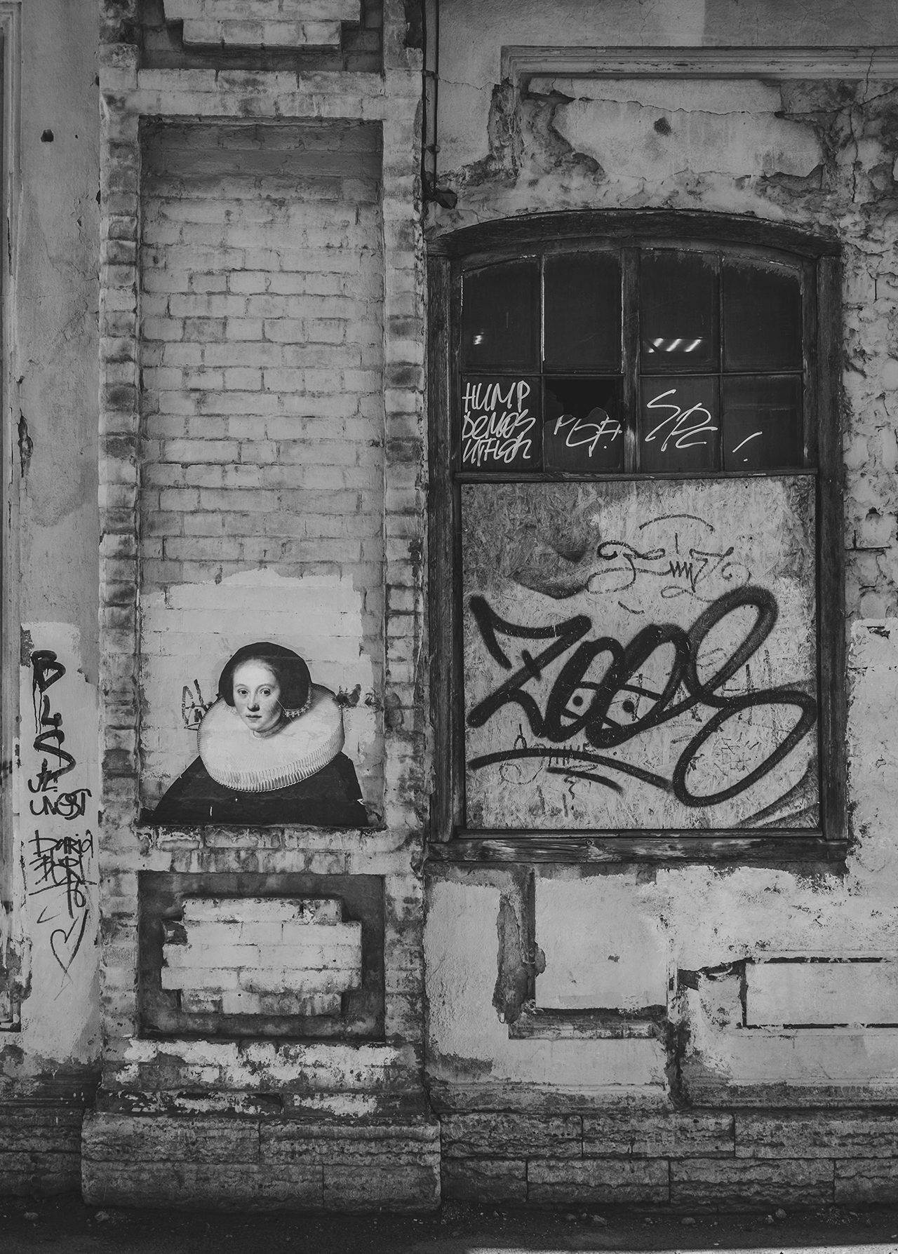 Monochrome image of brick wall art featuring a woman in a ruff collar next to a boarded window covered in graffiti in an urban setting.