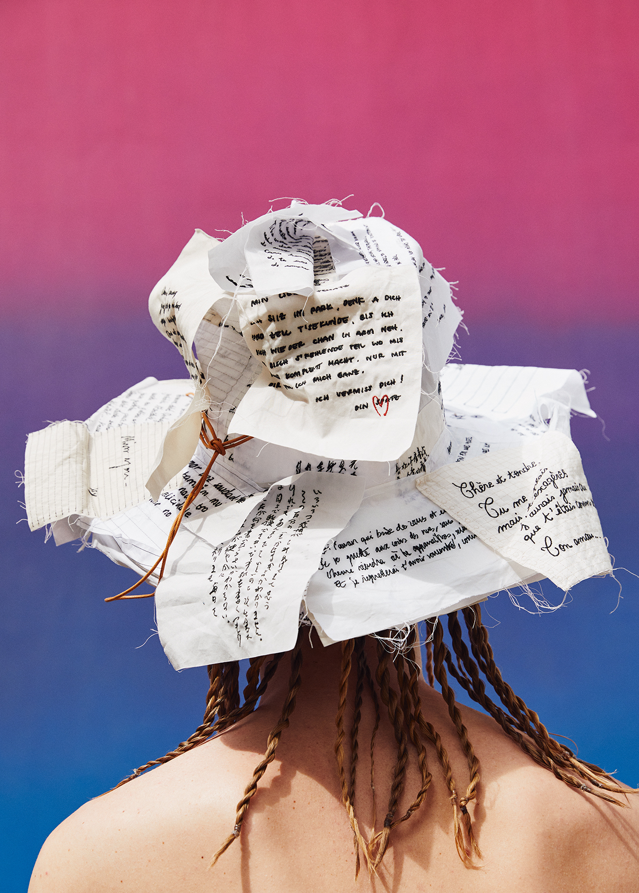 From behind, an individual models a hat constructed of handwritten notes against a color gradient background.
