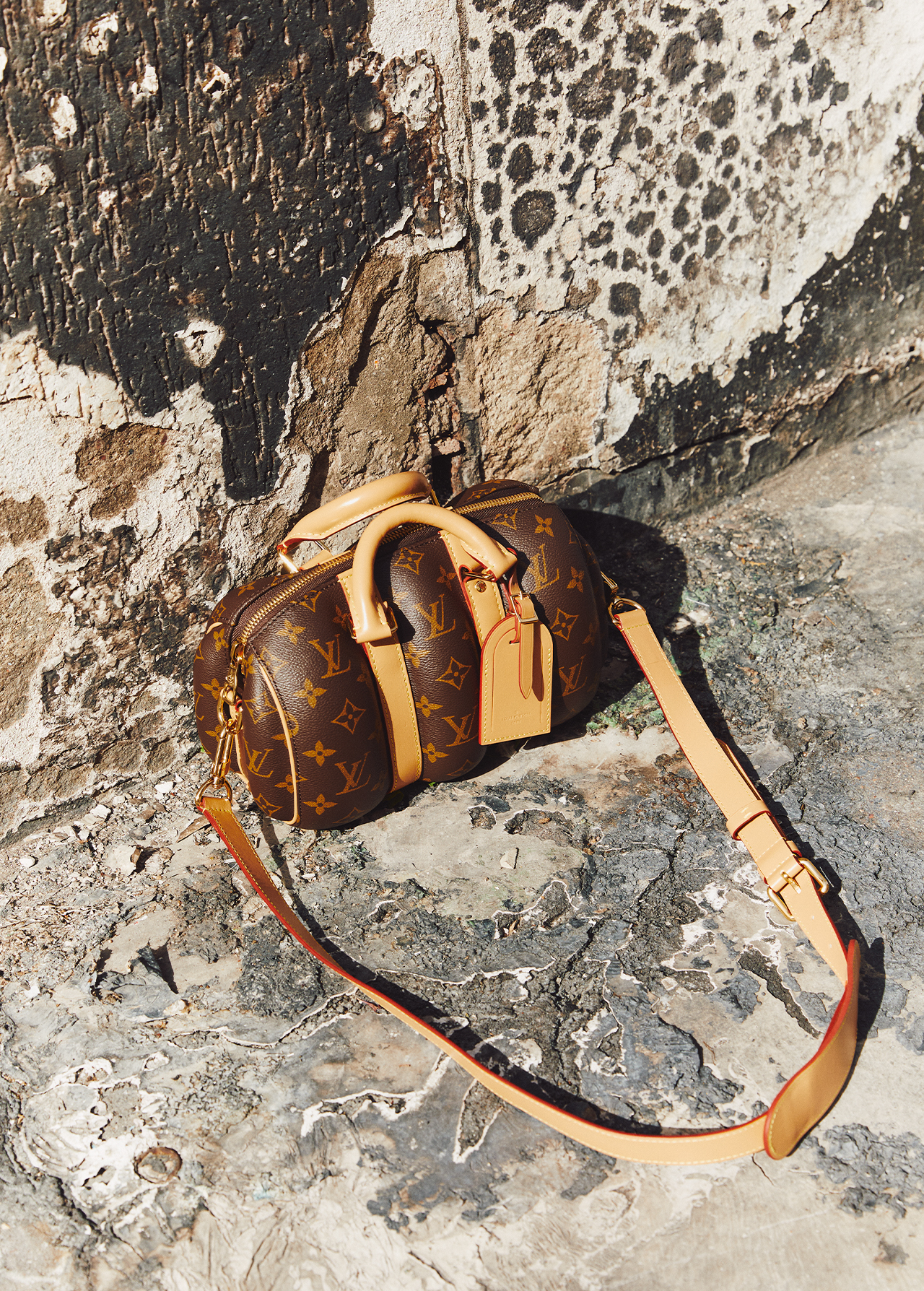 Louis Vuitton handbag with shoulder strap laying on an aged stone or concrete surface with mottled patterns and shadows, indoors.