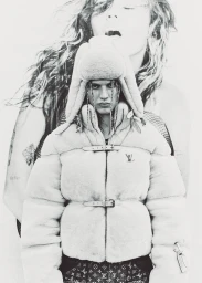 Monochrome fashion portrait of a model wearing a fluffy puffer jacket and trapper hat against a large background print