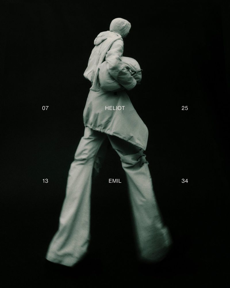 Person walking in loose fitting hooded jacket and pants against dark background, studio shot, fashion concept, muted tones.