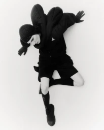 Model wearing black padded outerwear, knitted cap, and knee-high socks against a white studio background.