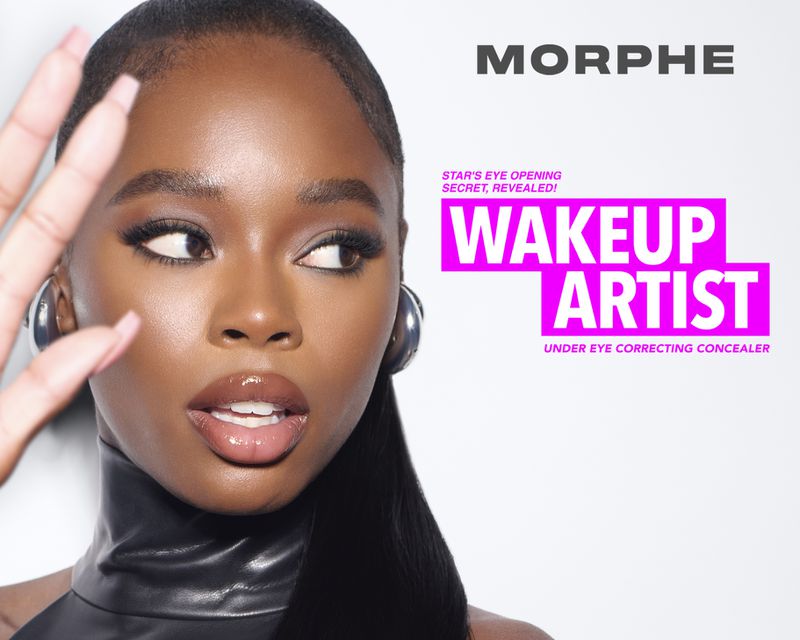 Close-up studio shot of a young black woman with glossy lips wearing a black top and silver hoop earrings against a bright background.