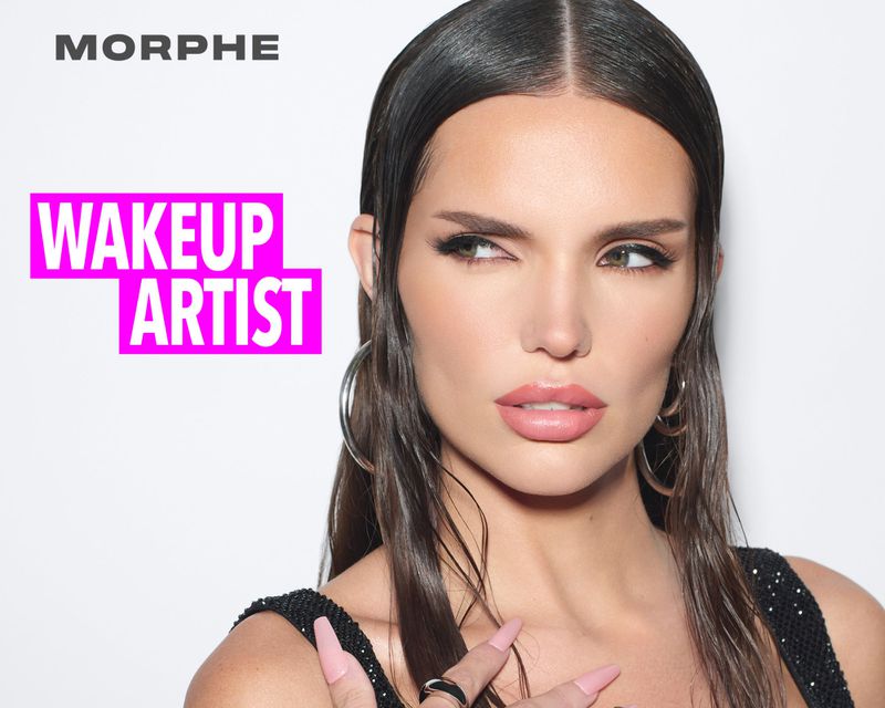 Close-up studio shot of a brunette woman with glam makeup, hoop earrings, and a black sequined top, looking to the side on a white background.