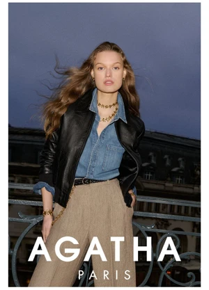 Model wearing a black leather jacket and denim shirt leaning against an ornate balcony railing outdoors at dusk.