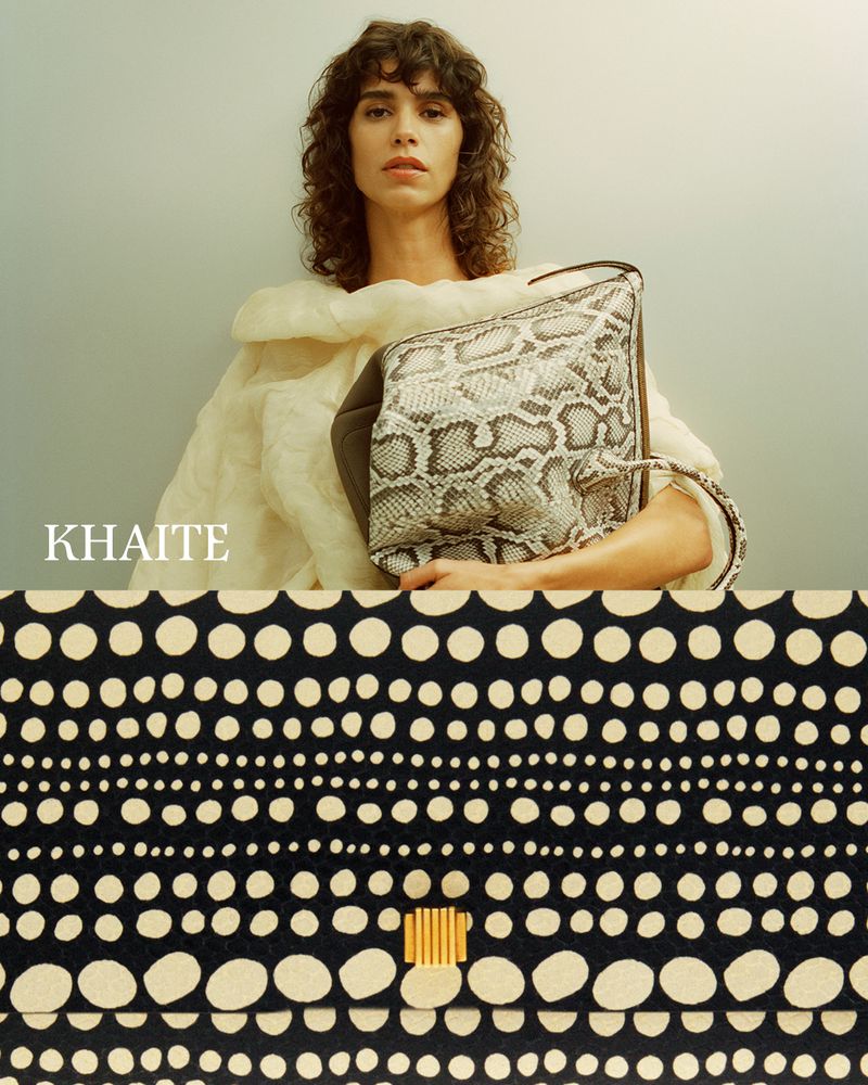 Fashion shot of a woman with curly brown hair holding a snakeskin-print handbag, posed in front of a black and white patterned background.