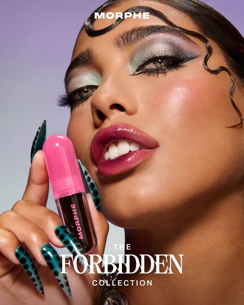 Close-up of a woman showcasing Morphe makeup, including colorful eyeshadow and glossy lips, holding a Morphe lip product.