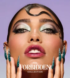 Close-up portrait of a woman with glossy pink lips, pastel eye shadow, and long stiletto nails against a purple backdrop.