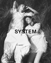 Two models lying down and resting among tall field grass in a monochrome fashion campaign photograph for System S/S 2025.