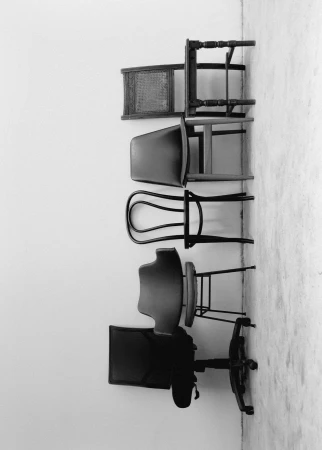 Monochrome image displaying a stacked collection of chairs against a solid white wall, creating an abstract composition with a focus on design.