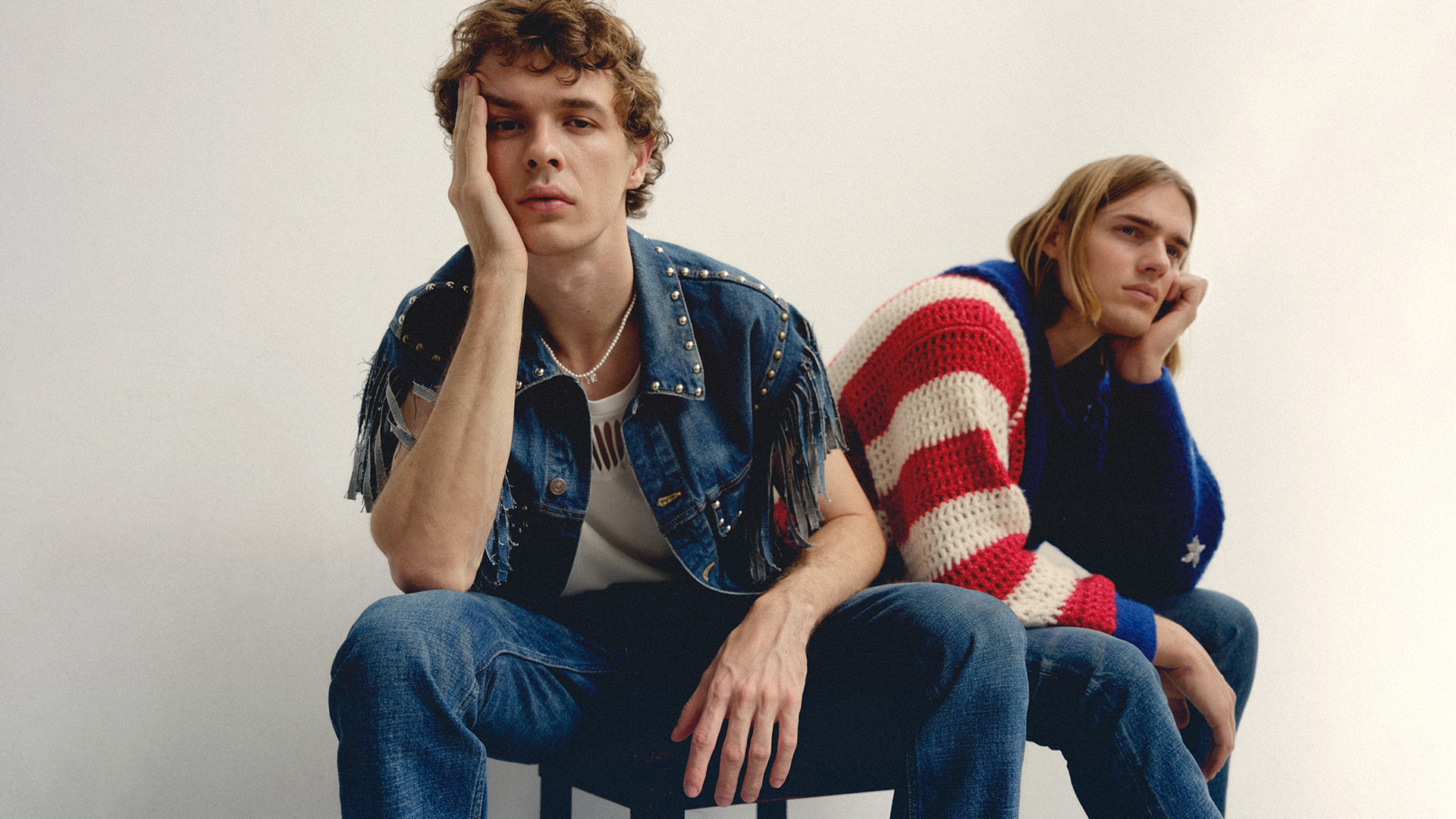 Two young male models seated against a plain white background wearing denim and patterned knitwear for Icon Magazine Australia