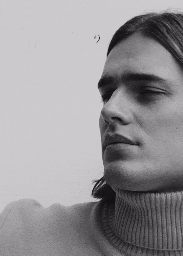 Close-up portrait of a man wearing a turtleneck sweater against a plain background in a black-and-white aesthetic.