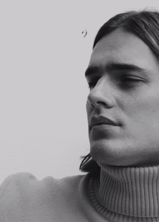 Close-up portrait of a man wearing a turtleneck sweater against a plain background in a black-and-white aesthetic.