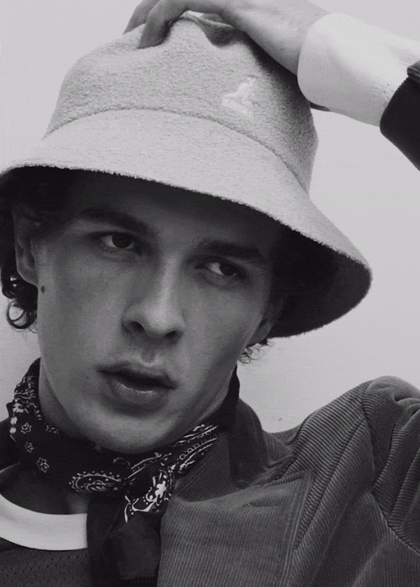 Close-up portrait of a man wearing a bucket hat and patterned neck scarf from the Waiting Room project by Justin Woo.