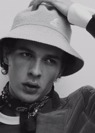 Close-up portrait of a man wearing a bucket hat and patterned neck scarf from the Waiting Room project by Justin Woo.