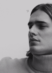 Close-up black and white portrait of a man wearing a turtleneck sweater against a plain background