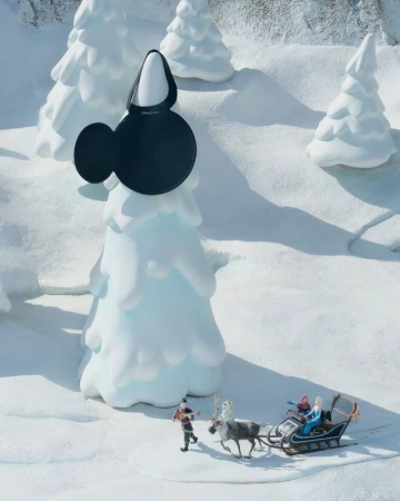 Winter holiday scene with a Minnie Mouse handbag on a snow-covered tree, a reindeer pulling a sleigh, and a figure walking in the snow.