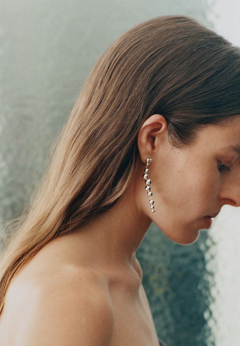 Close-up profile portrait of a woman wearing long silver beaded drop earrings for Georg Jensen S/S 25