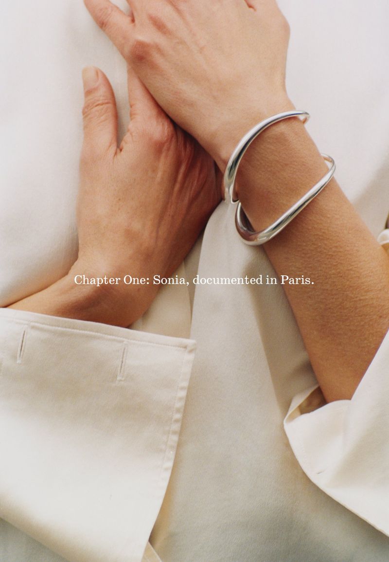 Closeup of a woman's hand and wrist with a silver bangle bracelet against a white background, studio lighting.
