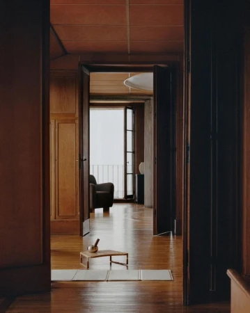Interior view through doorways of a minimalist home with hardwood floors, terra cotta colored walls, and view to outdoor balcony.