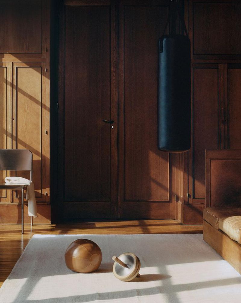 Interior shot of a room with a punching bag, wooden ball, and spinning top on a rug, with a chair and sofa in the background.