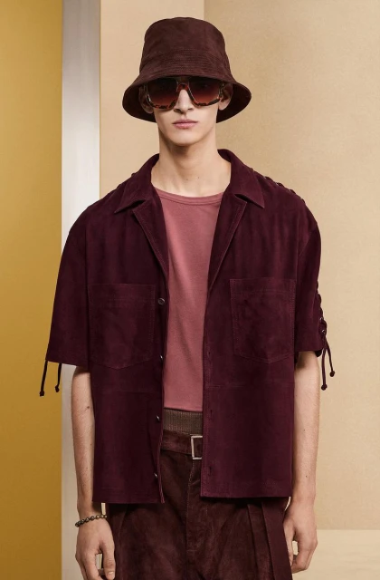A stylish adult male in brown coordinates poses indoors, wearing a bucket hat and sunglasses, creating a fashion-forward aesthetic.