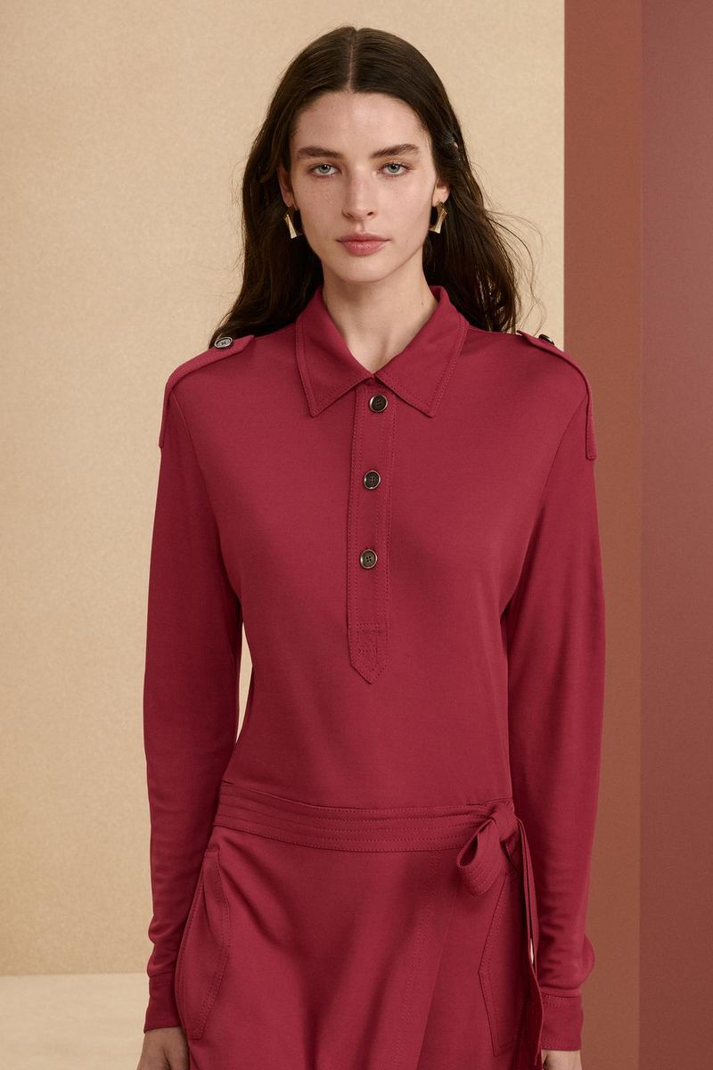 Brunette woman in a long-sleeved red dress with button details and jewelry, posing in a brightly lit studio setting, fashion portrait.
