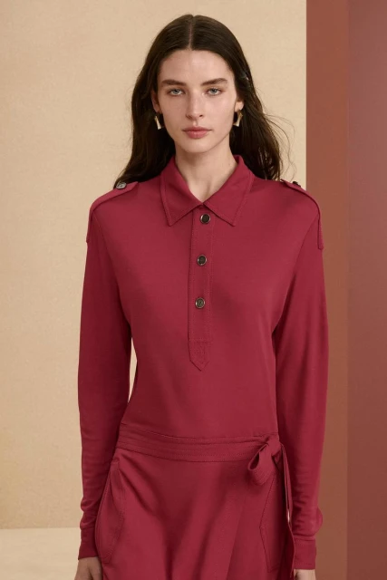 Brunette woman in a long-sleeved red dress with button details and jewelry, posing in a brightly lit studio setting, fashion portrait.