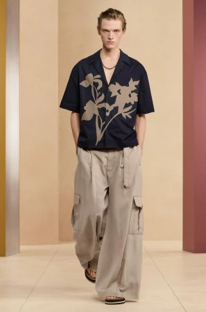 Male model in a dark navy patterned short-sleeve shirt and wide khaki trousers standing in a studio setting