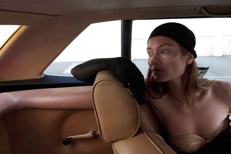 Elegant woman with a black headscarf and gloves in the back seat of a vintage car, exuding retro fashion style and sophistication.