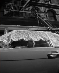 Model Jac Jagaciak seated in a car partially covered by a lace cloth, set against a New York building exterior for Magda Butrym.