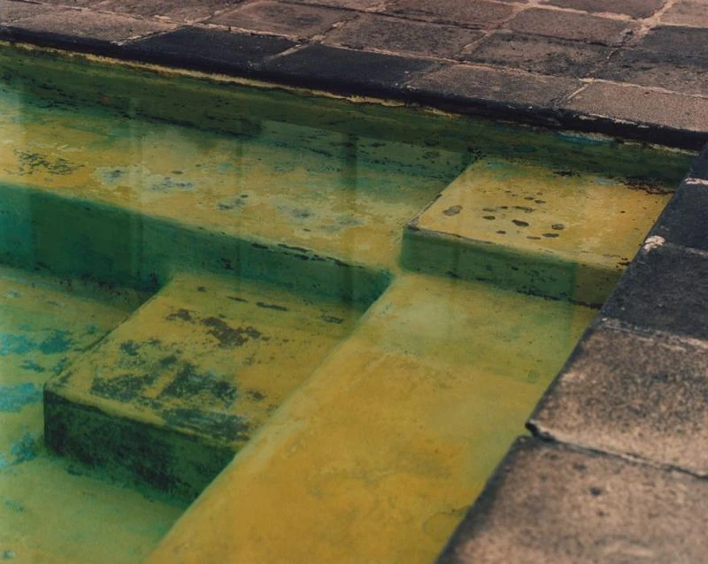 Tranquil steps descending into a swimming pool, featuring turquoise and yellow water with a stone tile border and steps.