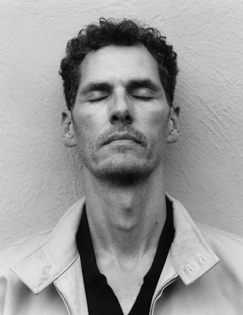 Close-up portrait of a man with eyes closed wearing a light jacket against a textured wall for Zara Origins